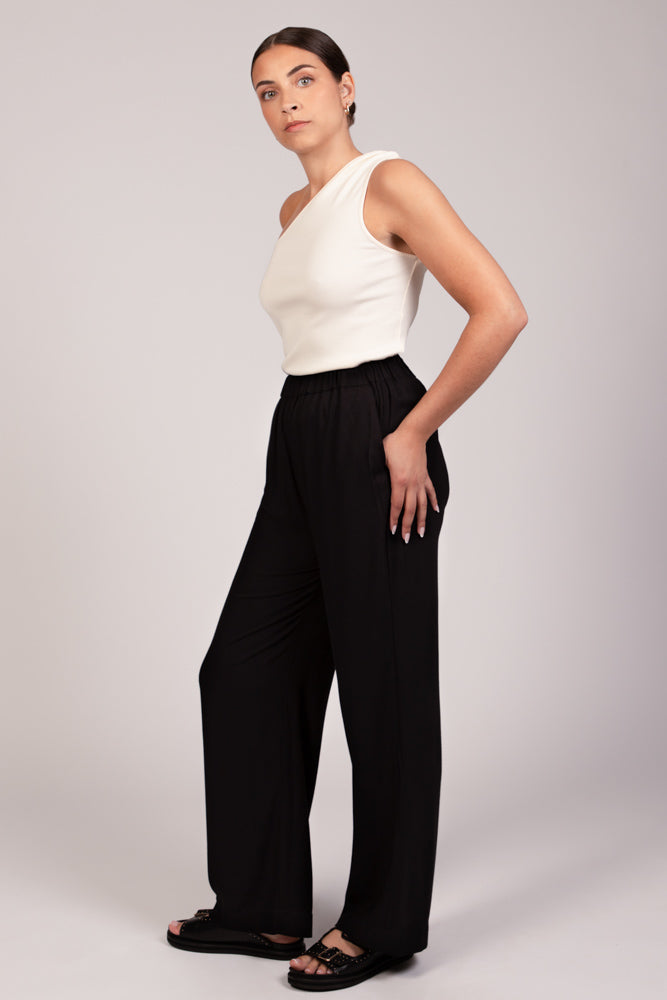Pantalon noir fluide taille élastique MILO, coupe droite confortable, porté avec le top NOVA asymétrique écru - collection été DILAA