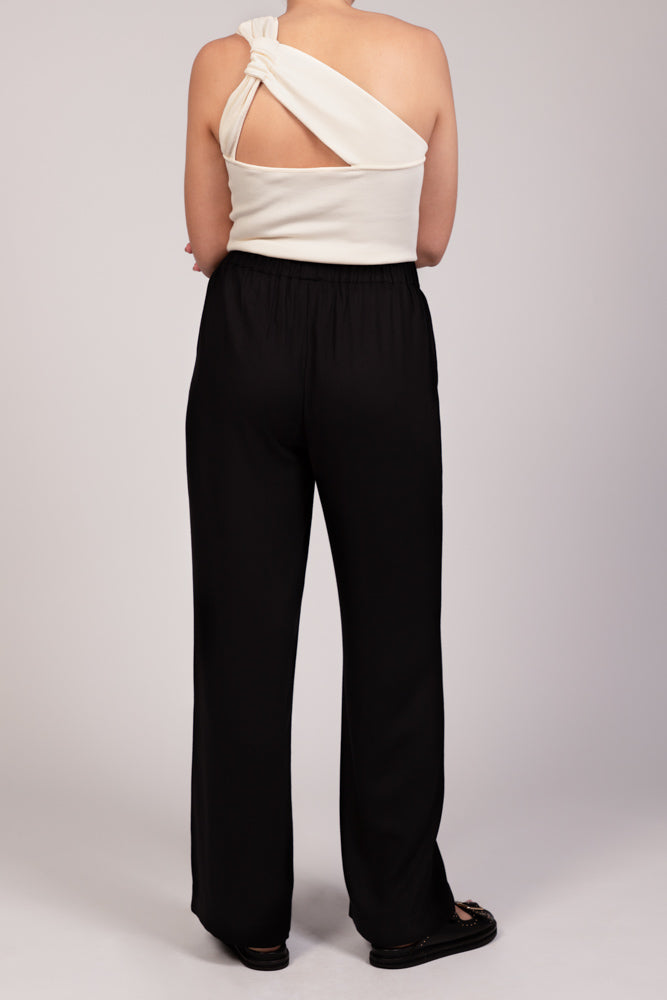 Pantalon noir fluide taille élastique MILO, coupe droite confortable, porté avec le top NOVA asymétrique écru, de dos - collection été DILAA