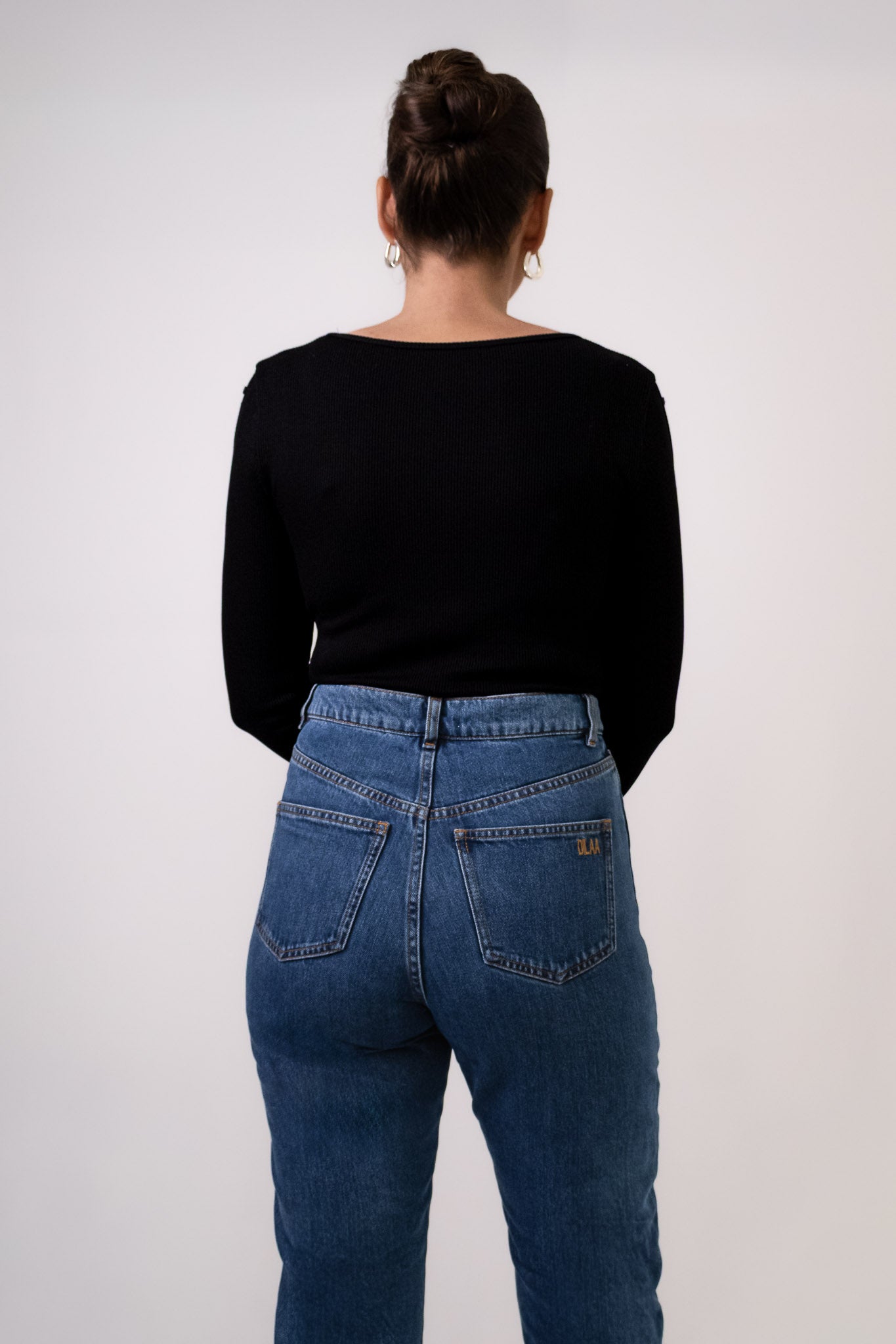 Top noir Soho en maille côtelée, col carré, avec détails découpés et boutonnés le long des manches, porté avec jean Pat taille haute. vue de dos. Marque DILAA